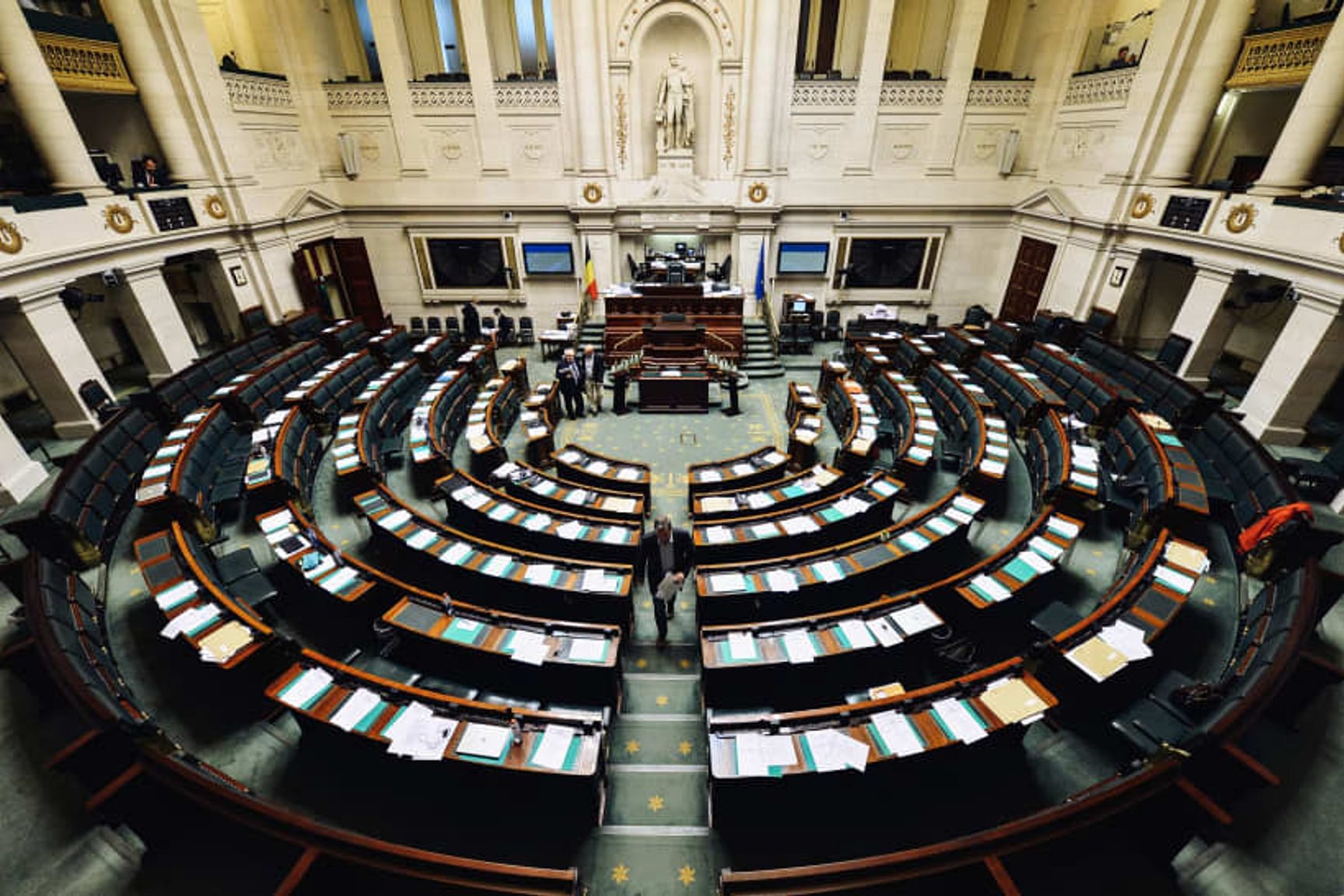 Parlementaire vergaderzaal met halfronde rijen zitplaatsen en bureaus, gezien van bovenaf.