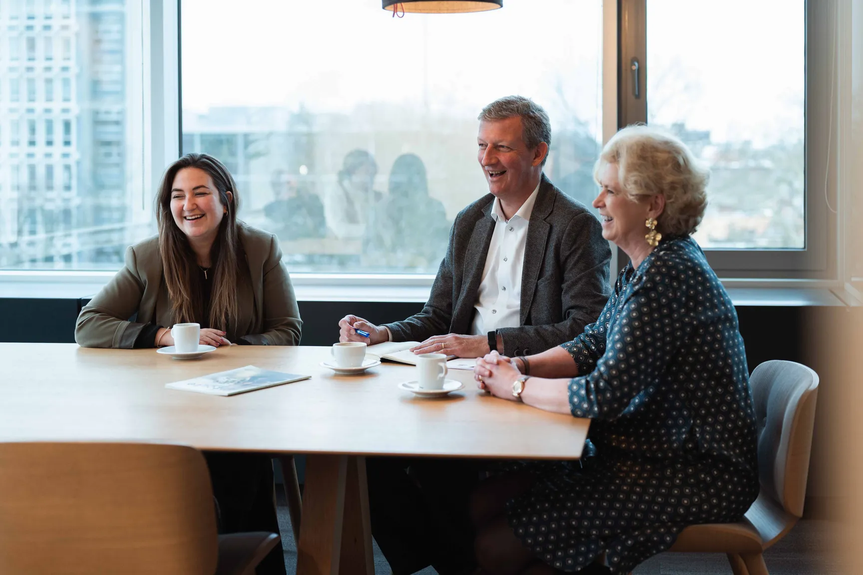 Foto van 3 personen die rond een tafel overleggen tijdens een strategische HR-meeting met focus op samenwerking en professionele groei.