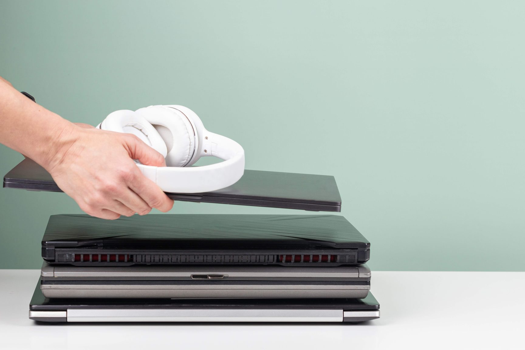 Een afbeelding van een aantal laptops die op elkaar zijn gestapeld met daarop een koptelefoon.
