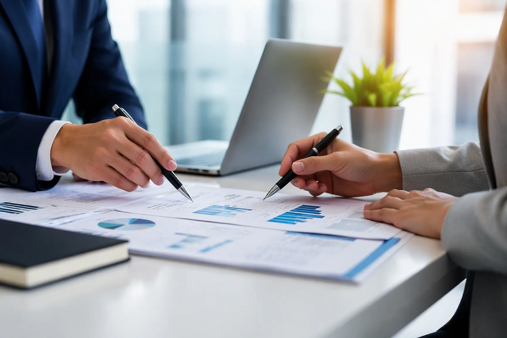 Twee personen bespreken financiële documenten en grafieken aan een vergadertafel in een kantooromgeving.