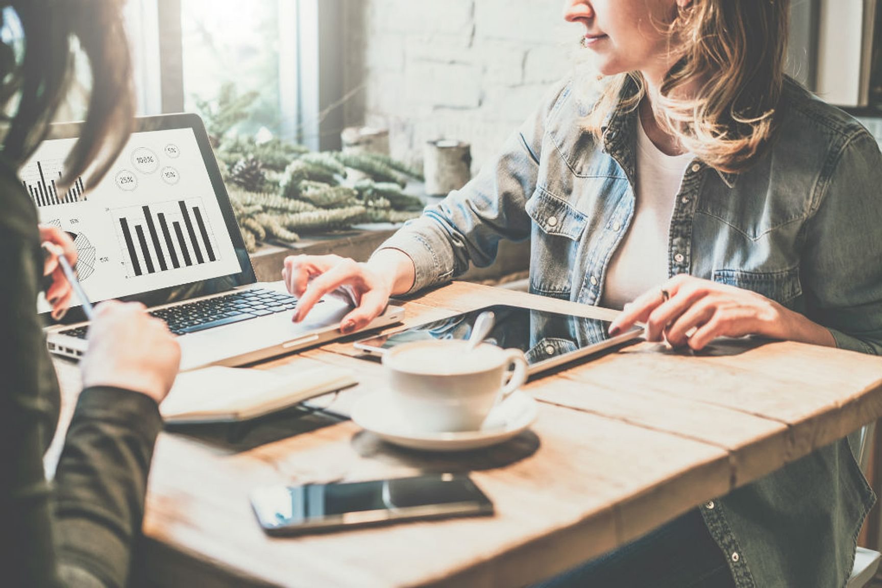 Twee personen werken samen aan een laptop met grafieken aan een tafel met een koffietas.