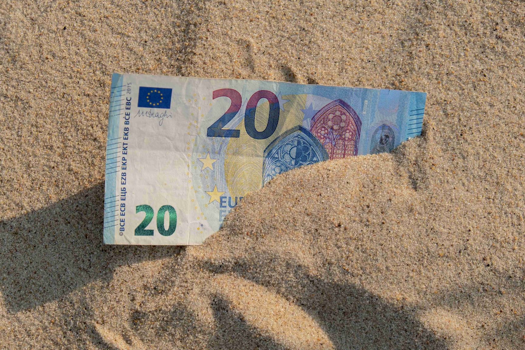 Een afbeelding van een 20 eurobiljet in het zand.