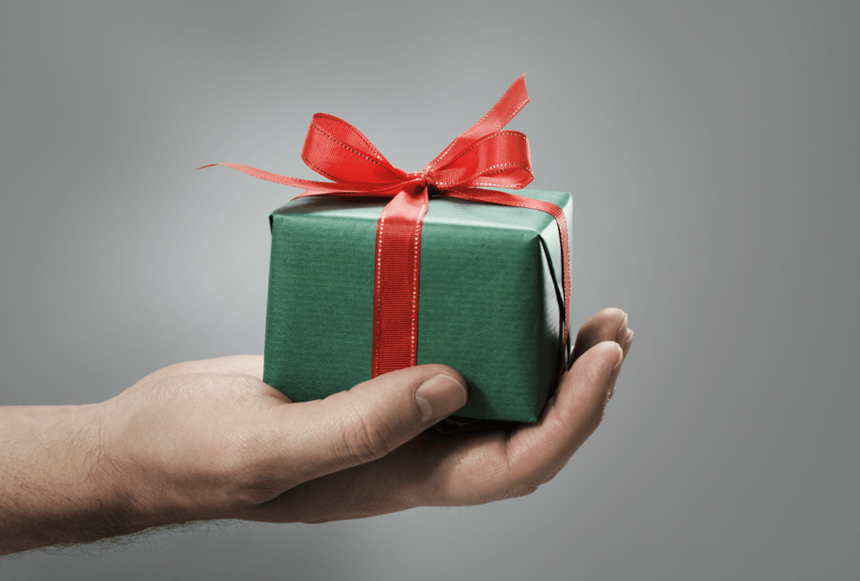 Hand die een klein geschenk met een rode strik vasthoudt tegen een neutrale achtergrond.