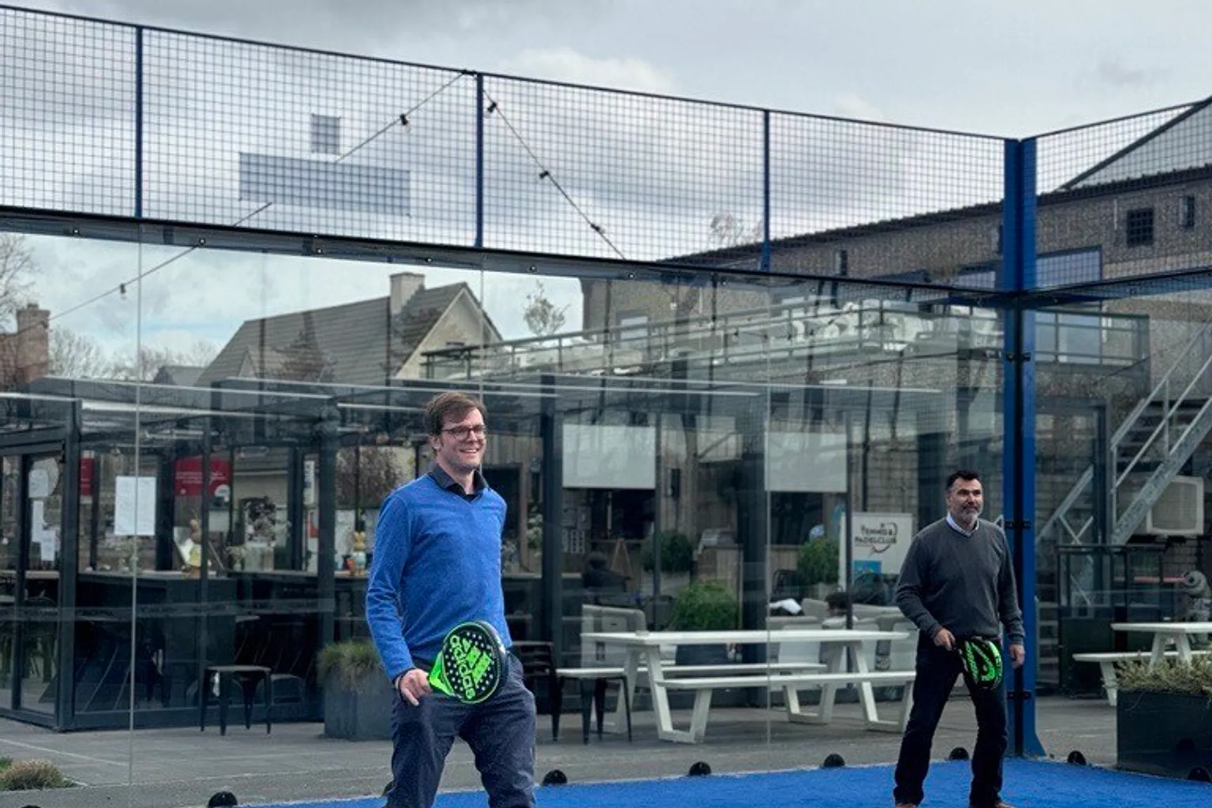 Afbeelding van twee personen die padel spelen op een buitenterrein.