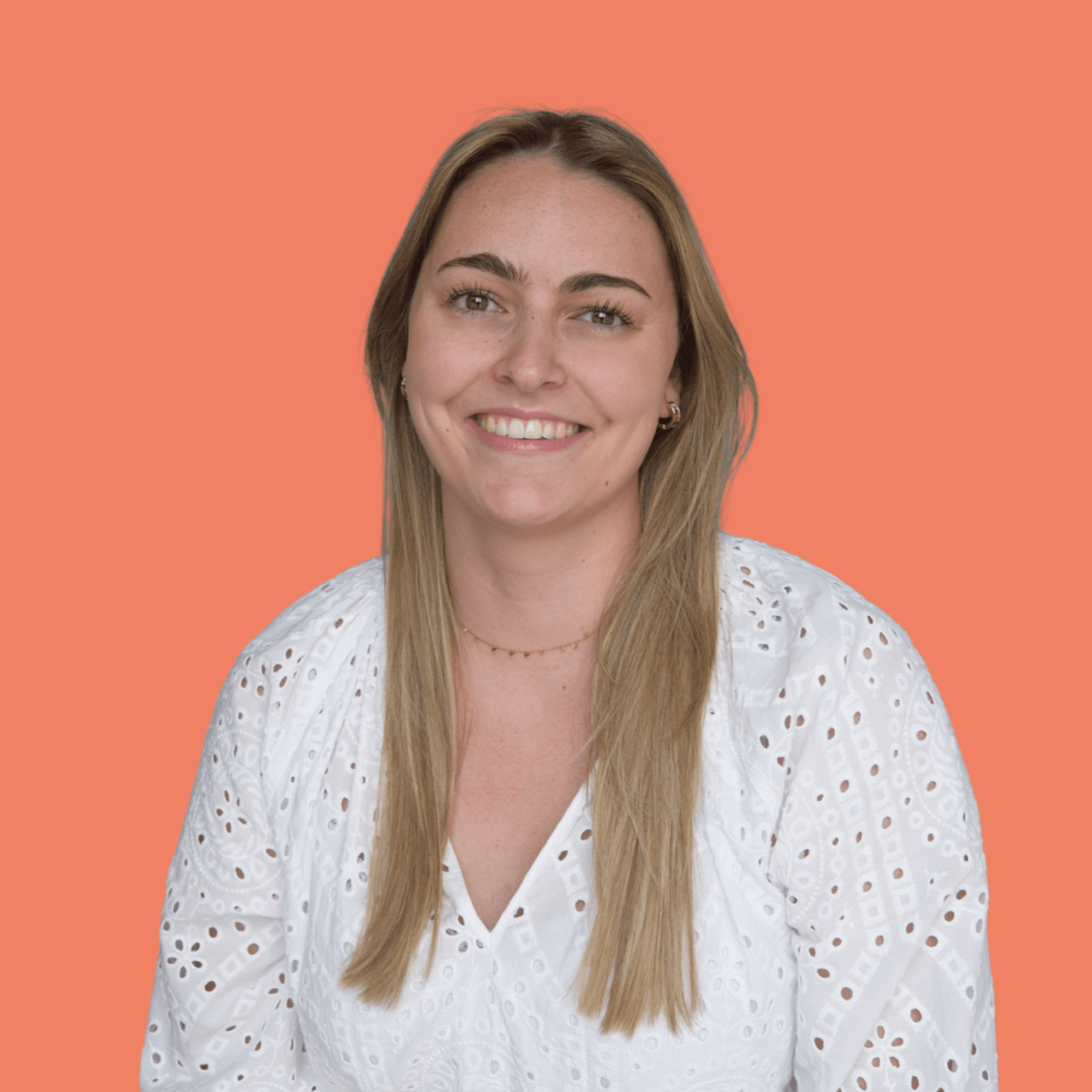 Onze collega Hanne kijkt met een warme glimlach recht in de camera. Ze draagt een witte blouse, heeft lang bruinblond haar en is springt uit beeld door middel van de oranje effen achtergrond.